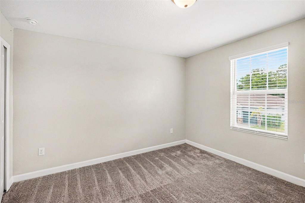 An empty bedroom features beige walls, gray carpet, and a window with white blinds — 490 BRUNSWICK DRIVE, DAVENPORT, FL