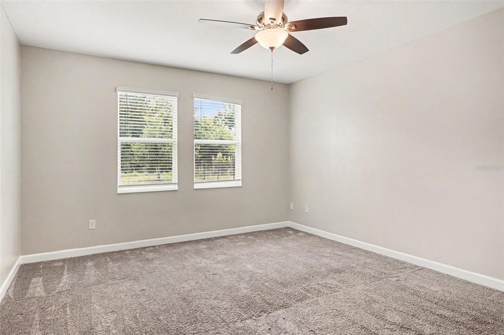 An empty bedroom features beige walls, gray carpeting, a ceiling fan, and two windows — 490 BRUNSWICK DRIVE, DAVENPORT, FL