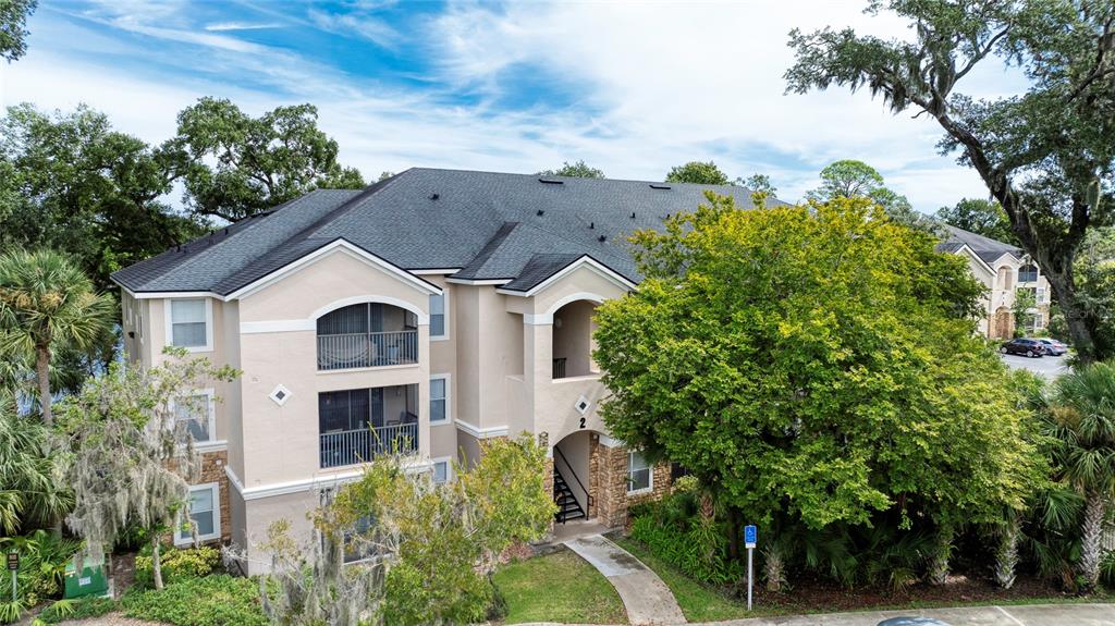 A three-story apartment building with a beige stucco exterior and a dark shingled roof — 940 VILLAGE TRAIL UNIT 2-207, PORT ORANGE, FL