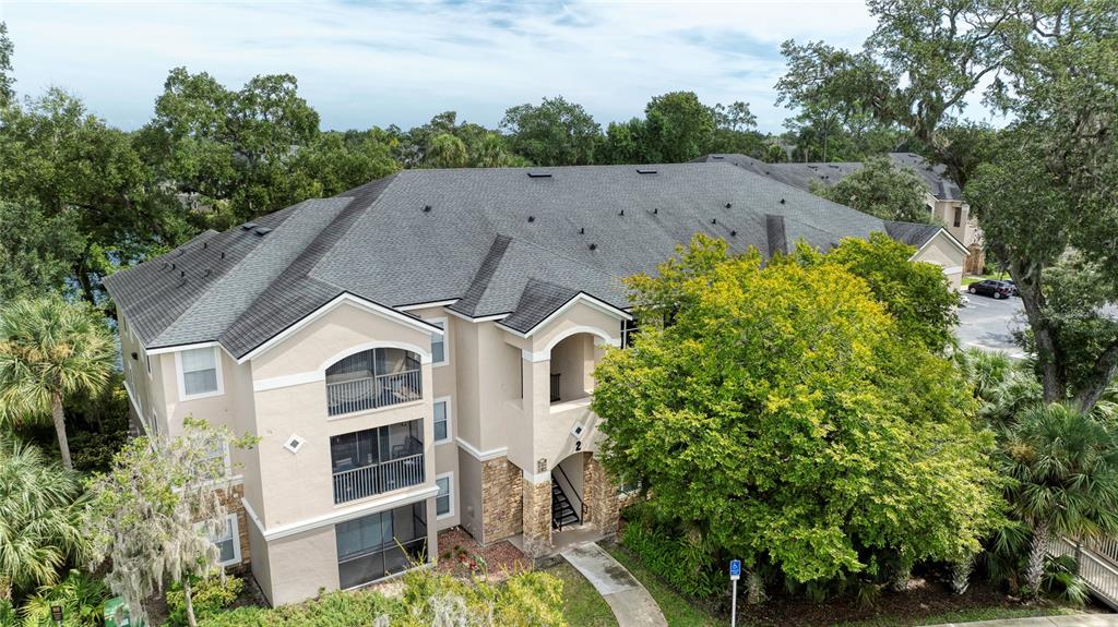 An aerial view of a three-story apartment building with a gray shingled roof — 940 VILLAGE TRAIL UNIT 2-207, PORT ORANGE, FL