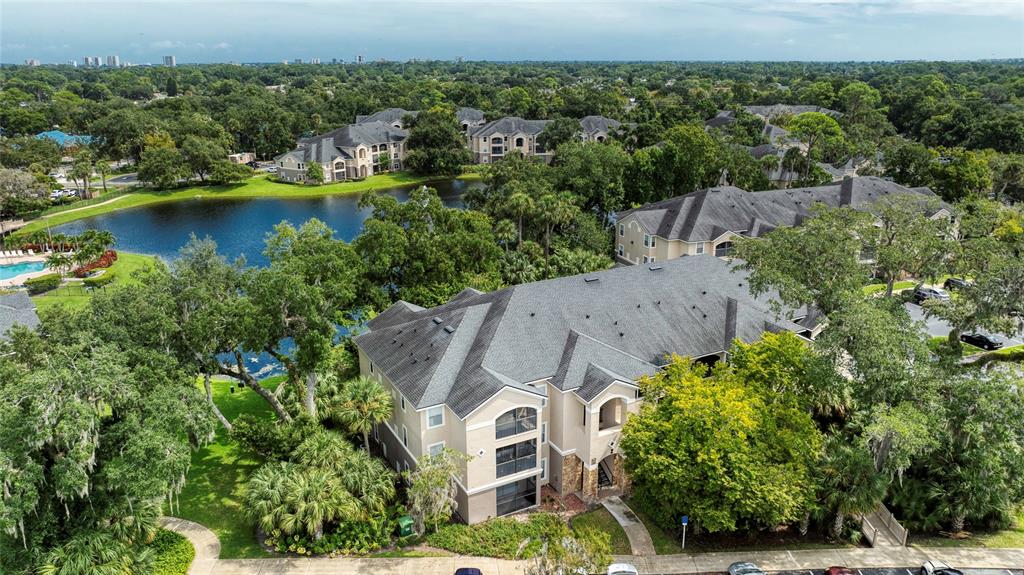 An aerial view shows a multi-story apartment building near a lake surrounded by trees — 940 VILLAGE TRAIL UNIT 2-207, PORT ORANGE, FL