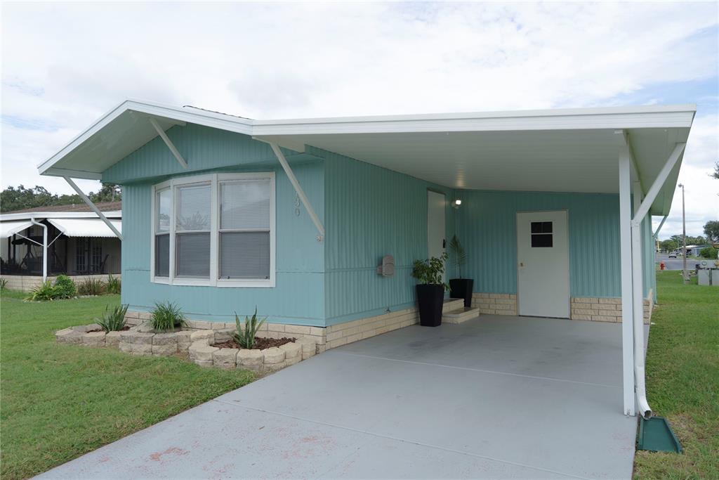 A light blue mobile home features a concrete driveway, a carport, and a stone planter — 3130 GREAT OAK STREET, WESLEY CHAPEL, FL
