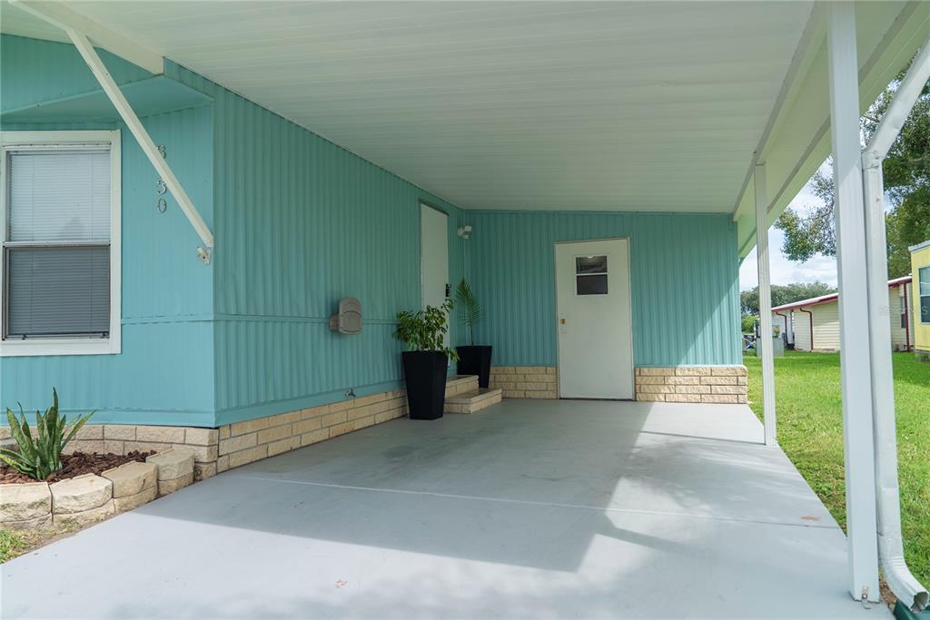 A teal mobile home features a covered carport with a concrete floor and brick skirting — 3130 GREAT OAK STREET, WESLEY CHAPEL, FL