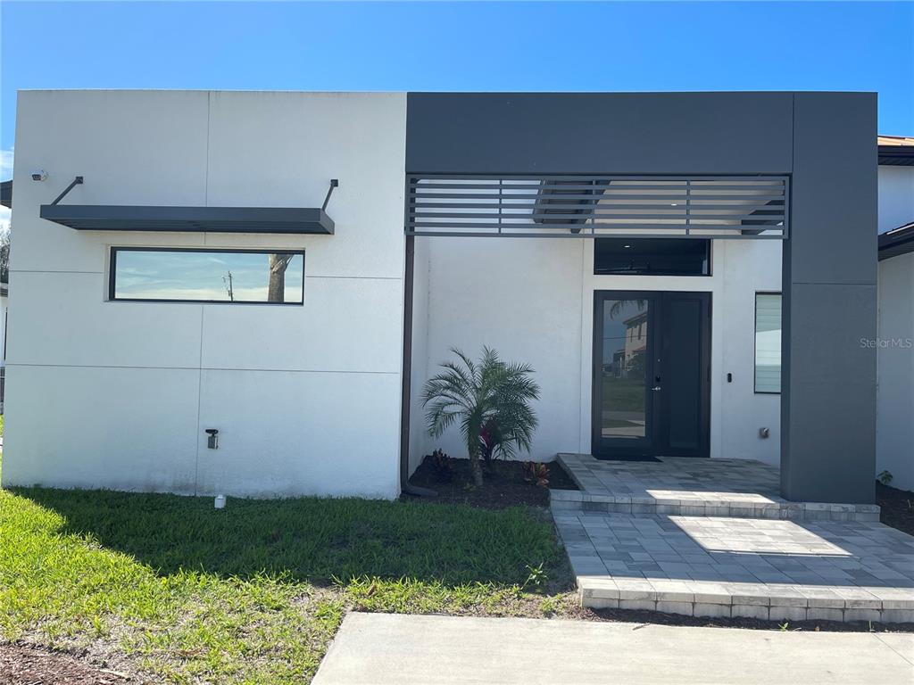 A modern house exterior features a white facade, a dark gray entryway, and a palm tree — 2106 SW 4TH STREET, CAPE CORAL, FL
