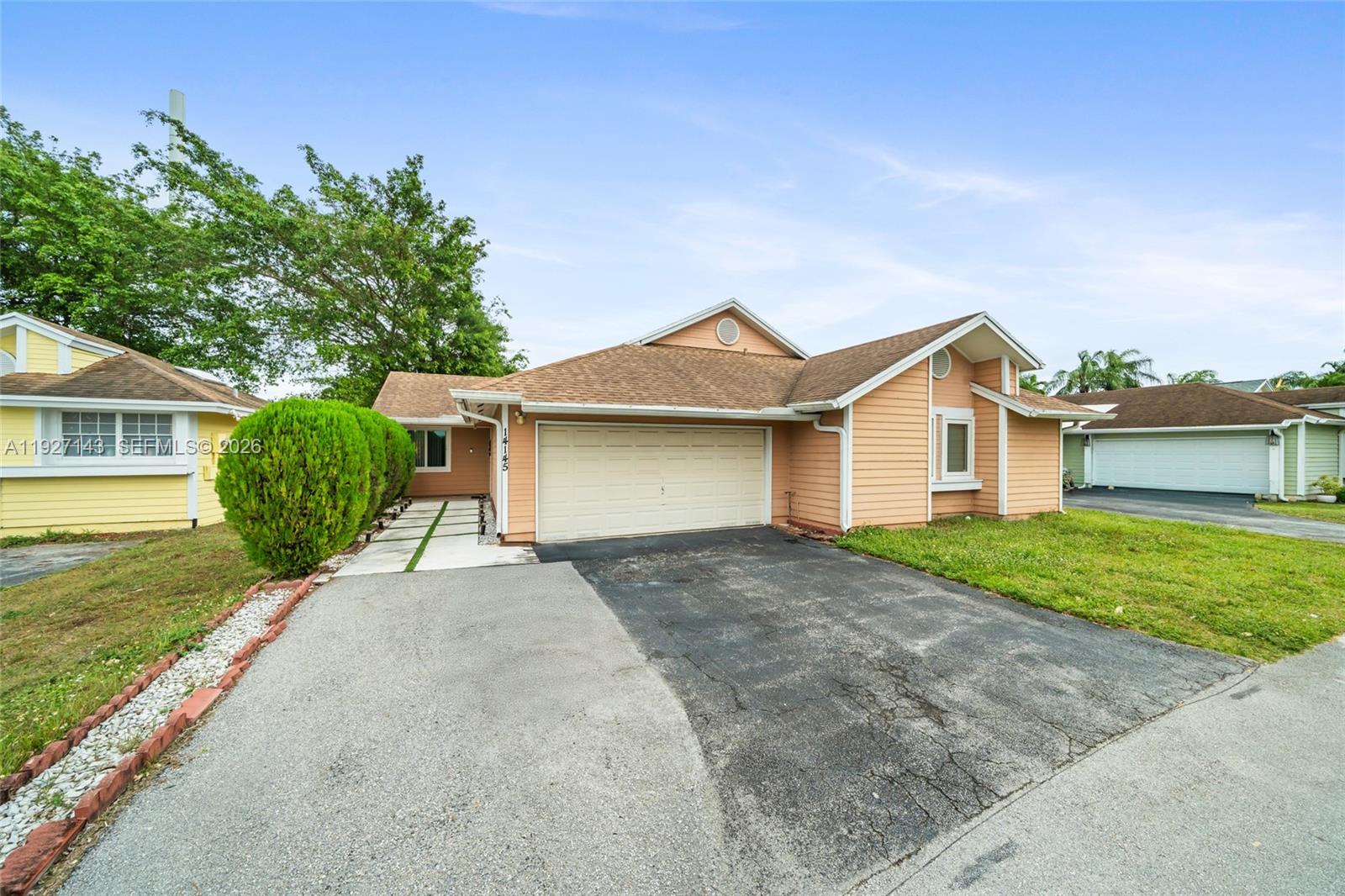 A peach-colored single-story house features a two-car garage and a paved driveway — 14145 SW 100th Ter, Miami FL 33186, MIAMI, FL