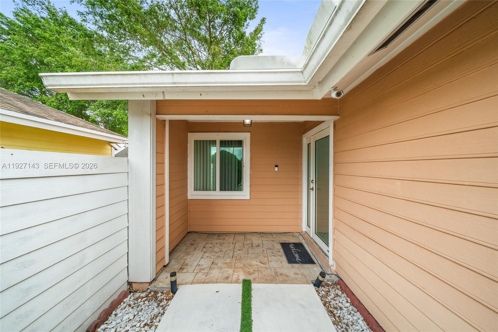 A covered patio features tan siding, a tiled floor, and a glass-paned entry door — 14145 SW 100th Ter, Miami FL 33186, MIAMI, FL
