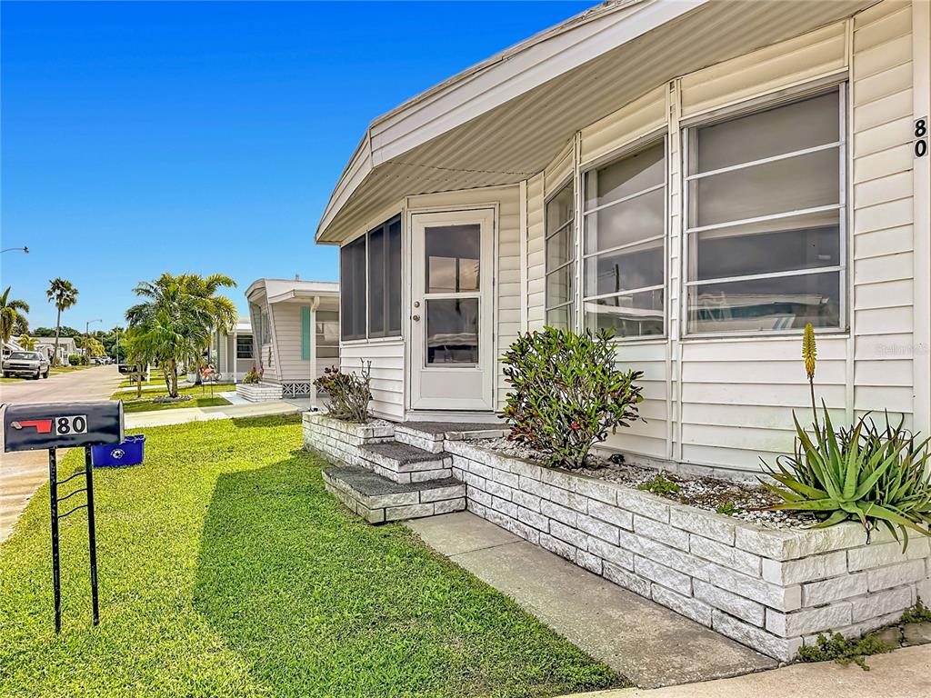 A white mobile home exterior features a stone planter, a front door, and a mailbox — 80 DEL RIO DRIVE, PALMETTO, FL