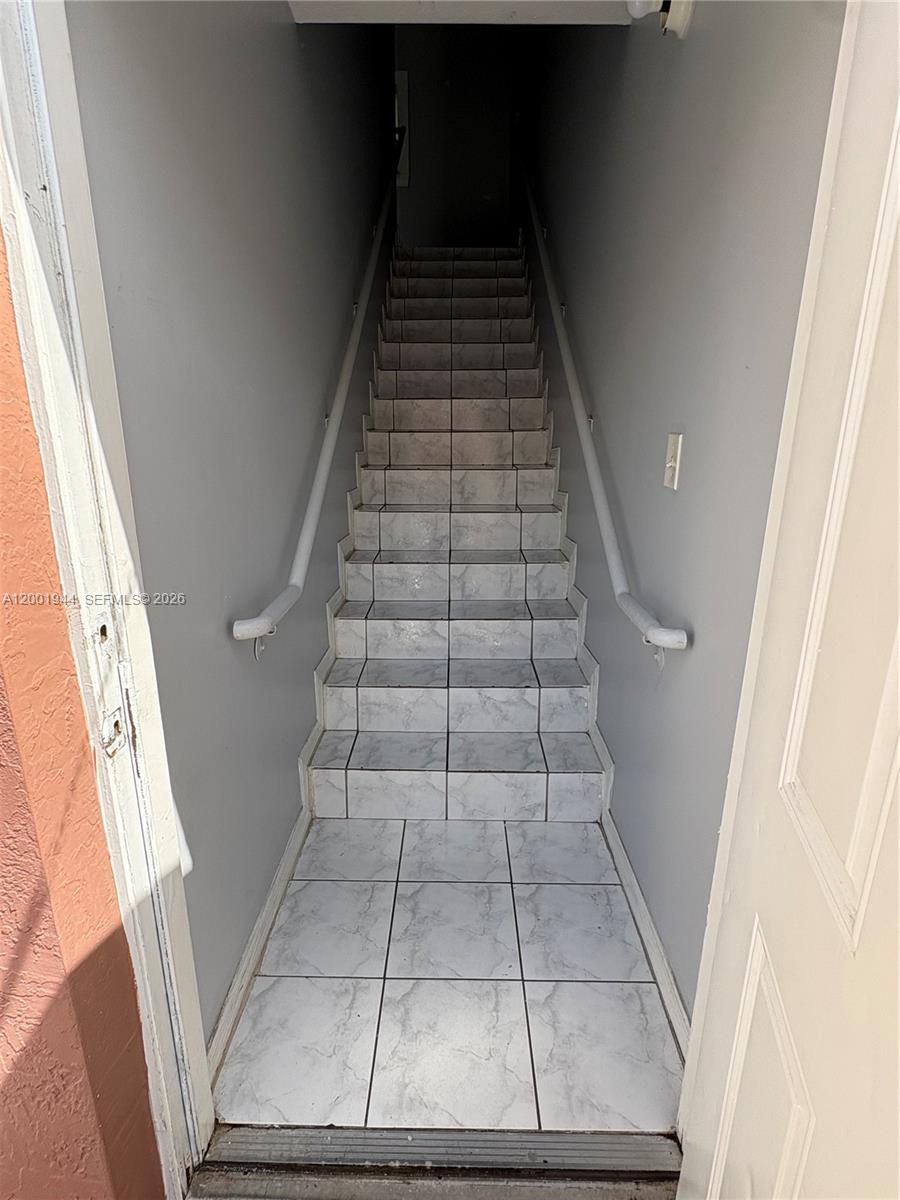 A narrow staircase with white marble-patterned tile leads upward between two gray walls — 12035 SW 14th St # 105, Miami FL 33184, MIAMI, FL