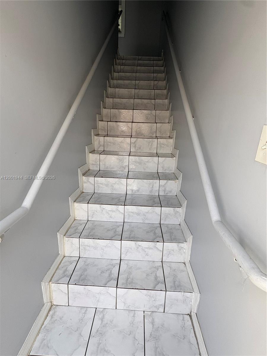 A straight staircase features white marble-patterned tile treads and risers with white handrails — 12035 SW 14th St # 105, Miami FL 33184, MIAMI, FL
