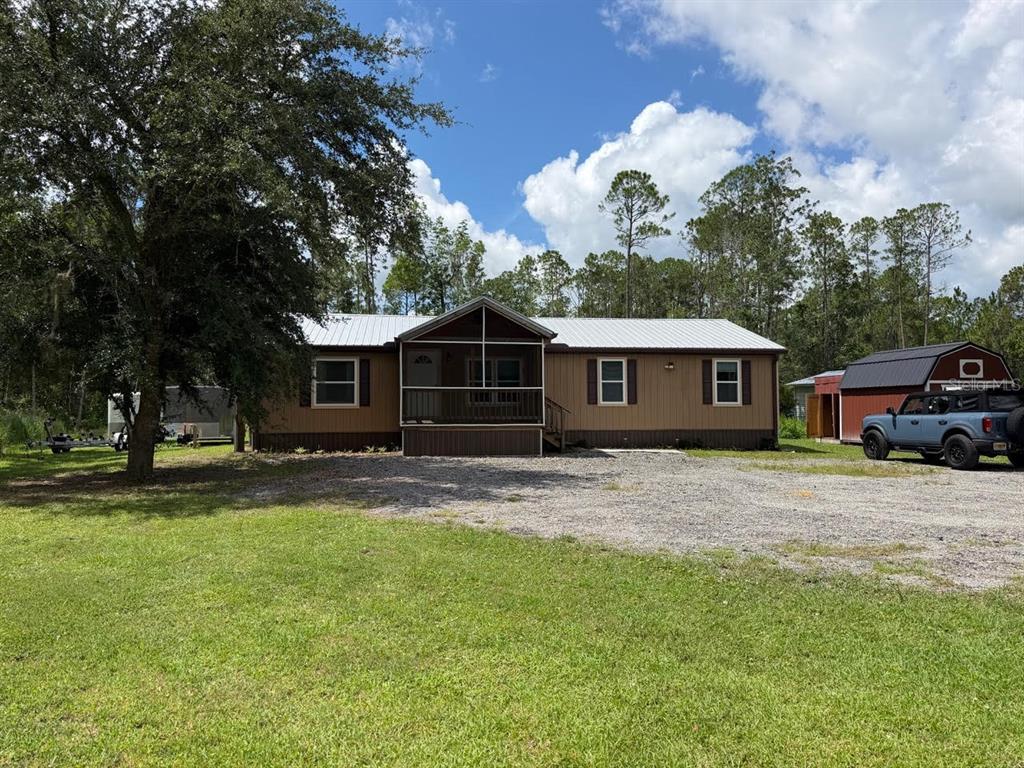 A tan manufactured home with a metal roof and a screened-in front porch — 5171 MAHOGANY BOULEVARD, BUNNELL, FL