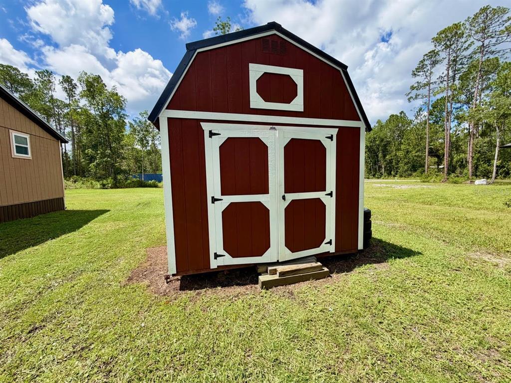 A single-story house with brown siding and a metal roof sits on a gravel lot — 5171 MAHOGANY BOULEVARD, BUNNELL, FL