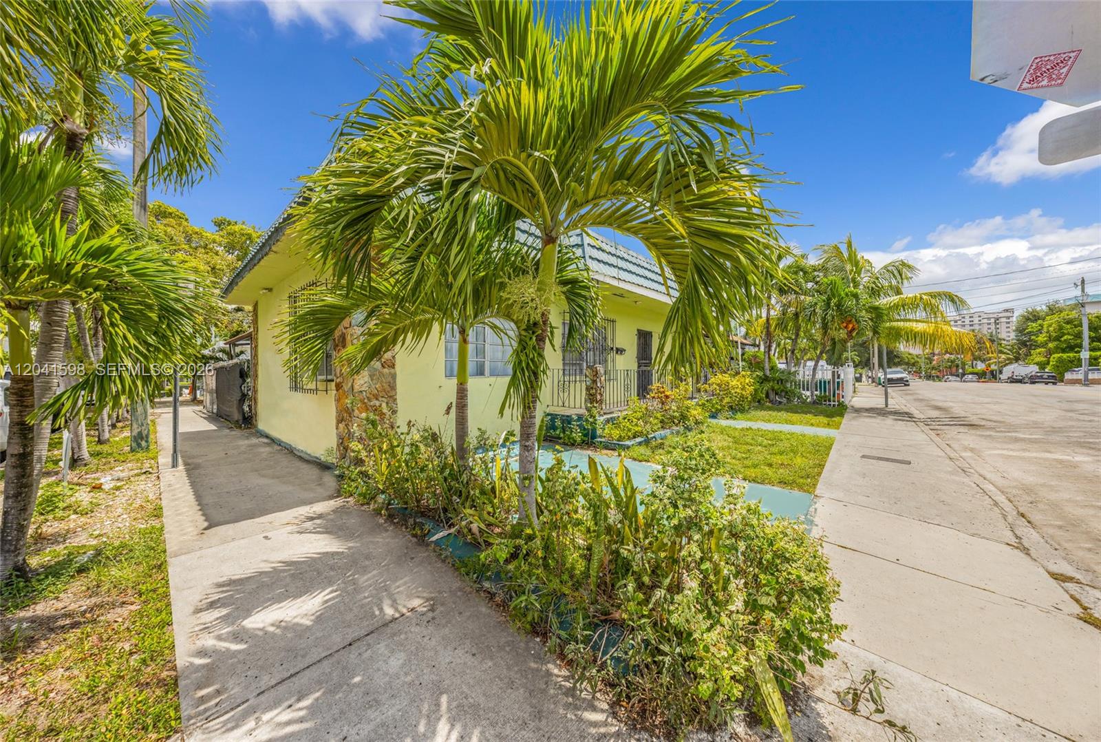 A light yellow house with a stone accent wall and palm trees sits near a sidewalk — 1477 NW 2nd St, Miami FL 33125, MIAMI, FL