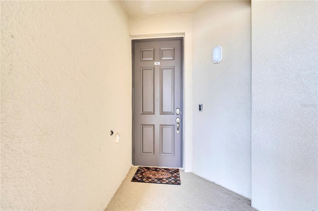 A gray front door with a welcome mat is set within a recessed entryway — 18114 GAWTHROP DRIVE UNIT 201, LAKEWOOD RANCH, FL