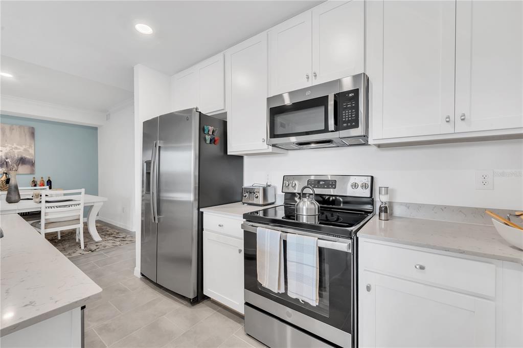 A modern kitchen features white cabinets, stainless steel appliances, and light-colored quartz countertops — 18114 GAWTHROP DRIVE UNIT 201, LAKEWOOD RANCH, FL