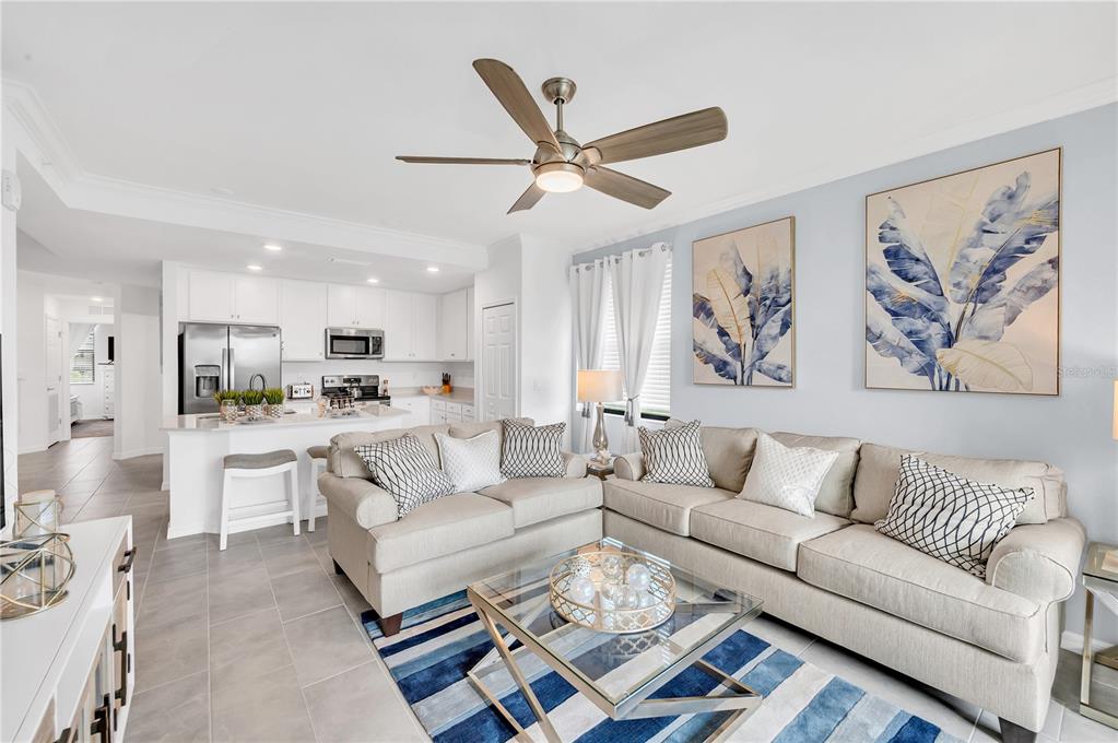 A living room with a beige sofa set, glass coffee table, and an open kitchen — 18114 GAWTHROP DRIVE UNIT 201, LAKEWOOD RANCH, FL