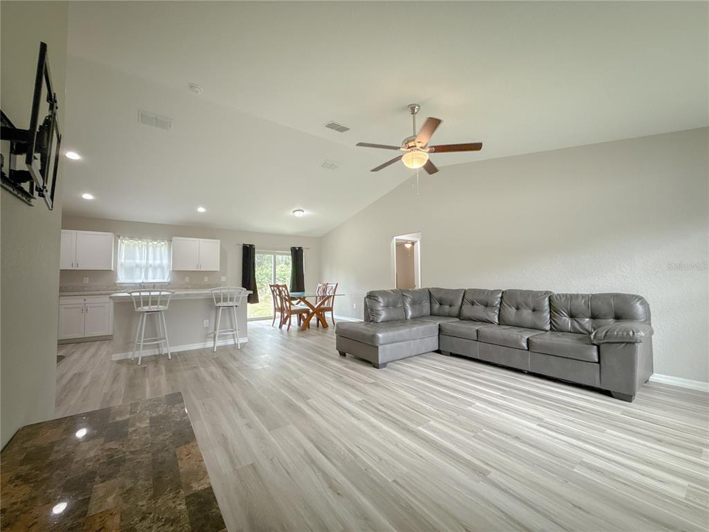 An open-concept living and dining area features gray wood-look flooring and a sectional sofa — 15434 SW 29TH TERRACE ROAD, OCALA, FL