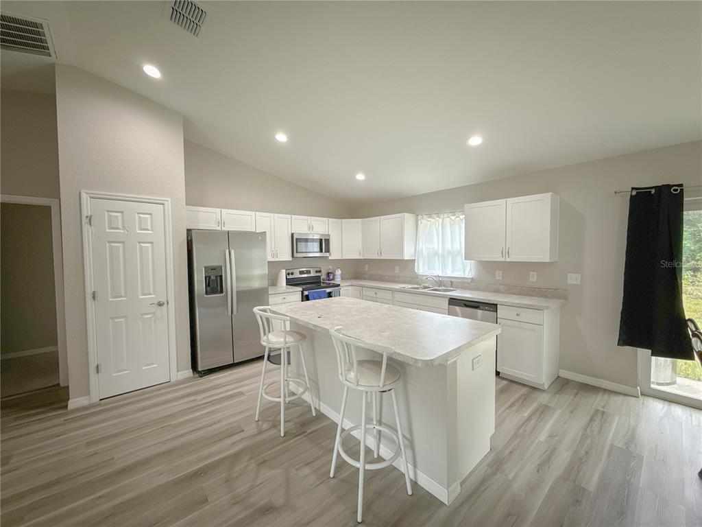 A kitchen with white cabinets, stainless steel appliances, a center island, and light wood flooring — 15434 SW 29TH TERRACE ROAD, OCALA, FL