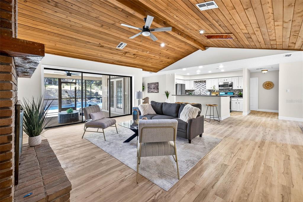 A living room with a wood-plank vaulted ceiling, brick fireplace, and an open kitchen — 14252 TRINITY ROAD, BROOKSVILLE, FL