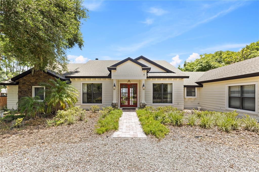 A single-story house with a stone facade and gravel driveway sits under large oak trees — 10355 TROUT ROAD, ORLANDO, FL