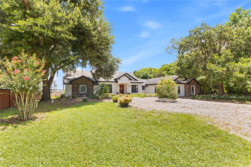 A single-story house with stone accents, light siding, and a gravel driveway under large trees — 10355 TROUT ROAD, ORLANDO, FL