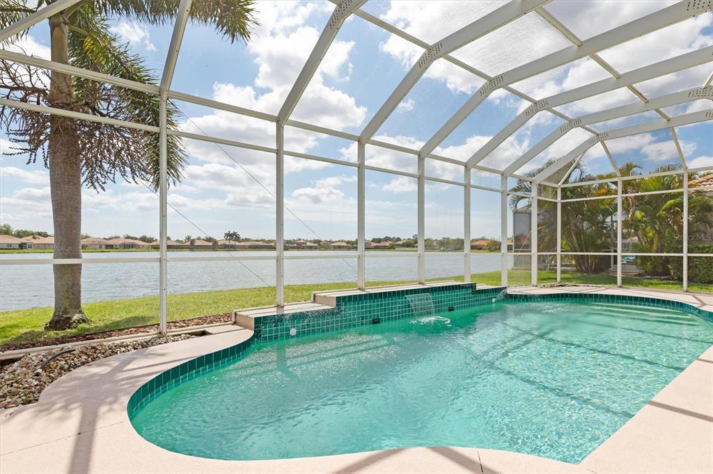 A screened-in swimming pool with a tiled water feature overlooks a lake and residential homes — 6918 74TH STREET CIRCLE E, BRADENTON, FL