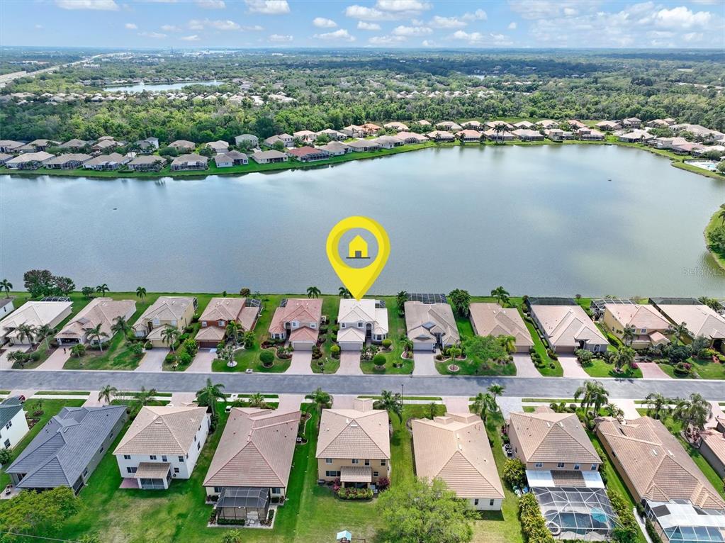 An aerial view shows a residential neighborhood with houses situated along a large lake — 6918 74TH STREET CIRCLE E, BRADENTON, FL