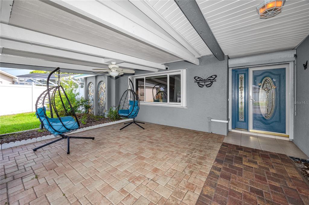 A covered patio features paver flooring, two hanging chairs, and a blue front door — 12291 MONARCH CIRCLE, SEMINOLE, FL