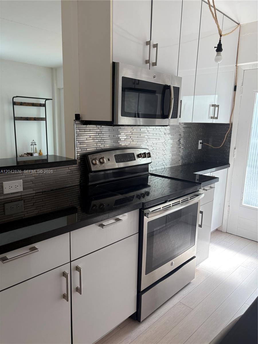 A kitchen features white cabinets, stainless steel appliances, black countertops, and a gray tiled backsplash — 1545 Euclid Ave # 2F, Miami Beach FL 33139, MIAMI BEACH, FL