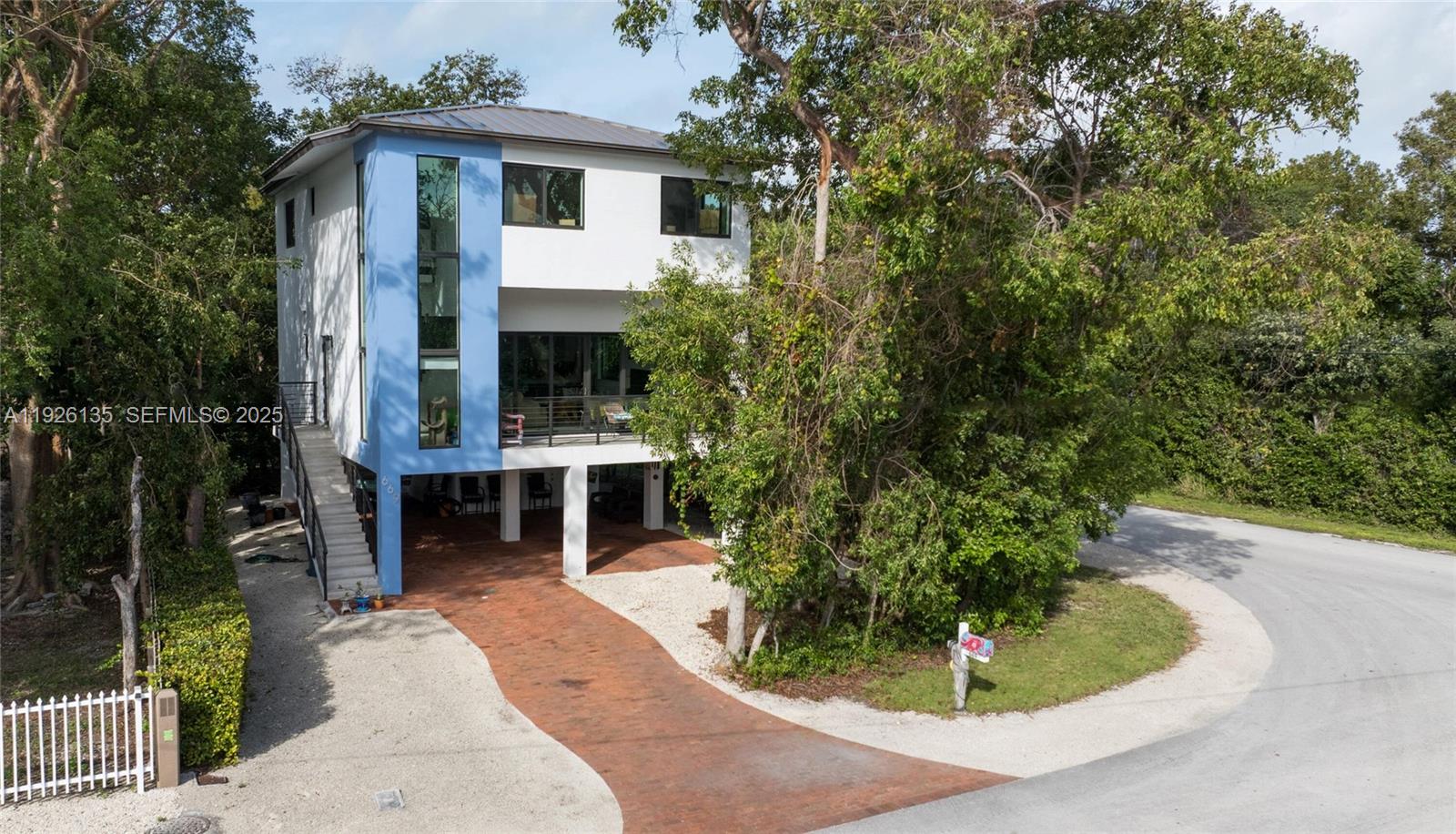 A modern two-story house with a blue accent wall stands on stilts above a driveway — 669 Colson Dr, Key Largo FL 33037, KEY LARGO, FL