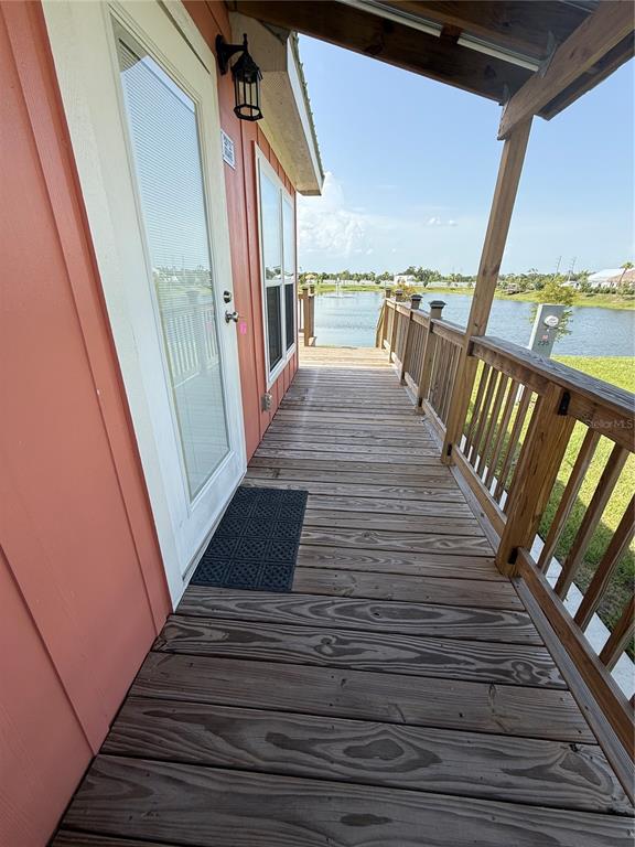 A wooden deck with a railing overlooks a pond next to a peach-colored house — 235 CLUB LANE UNIT 235, PUNTA GORDA, FL