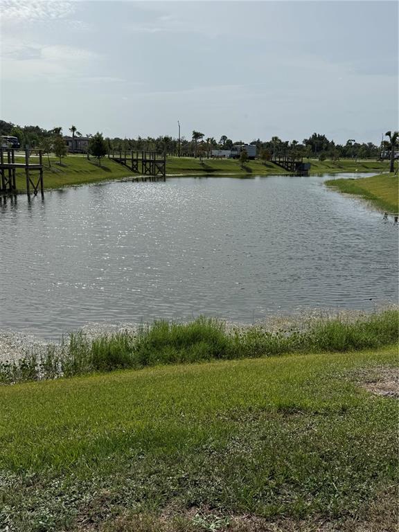 A grassy bank overlooks a pond with wooden docks and distant RVs under a sky — 235 CLUB LANE UNIT 235, PUNTA GORDA, FL