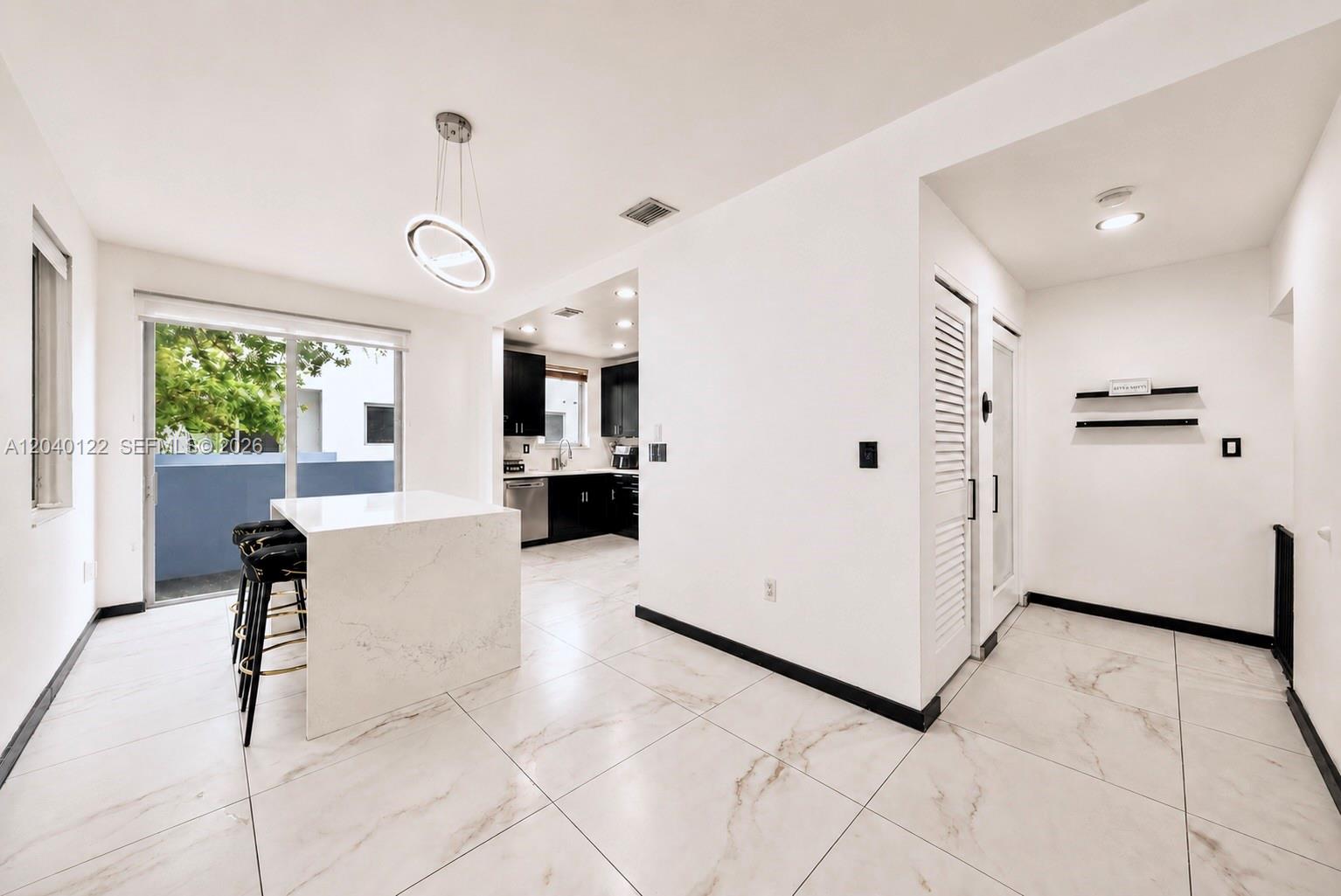A modern kitchen features a white marble island, black cabinetry, and light-colored tiled flooring — 193 N Shore Dr # 6, Miami Beach FL 33141, MIAMI BEACH, FL