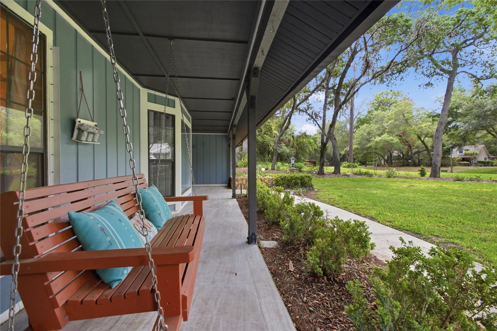 A covered porch features a wooden swing, blue siding, and a view of a grassy yard — 128 W GREENTREE LANE, LAKE MARY, FL