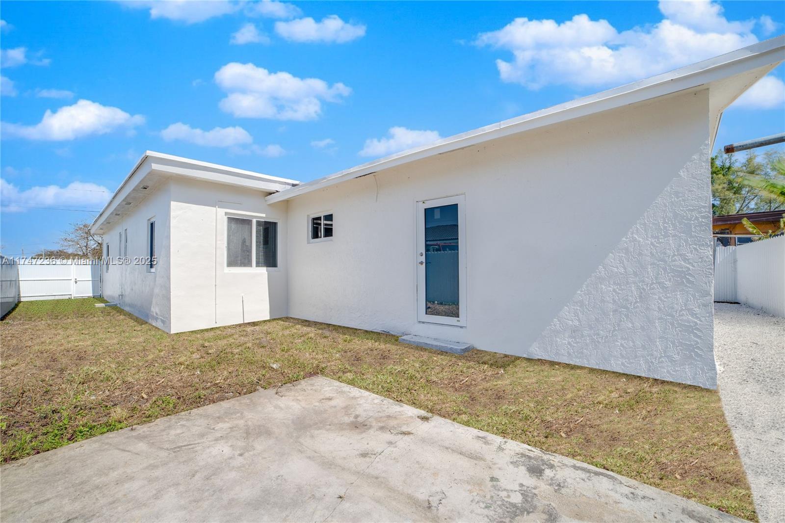 The exterior of a white stucco house features a concrete patio and a glass door — 10272 SW 178th St # 1, Miami FL 33157, MIAMI, FL