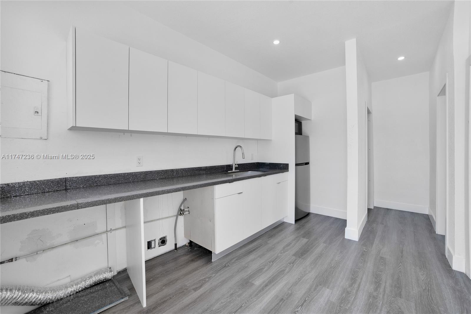 A minimalist kitchen features white cabinets, a dark speckled countertop, and grey wood-look flooring — 10272 SW 178th St # 1, Miami FL 33157, MIAMI, FL
