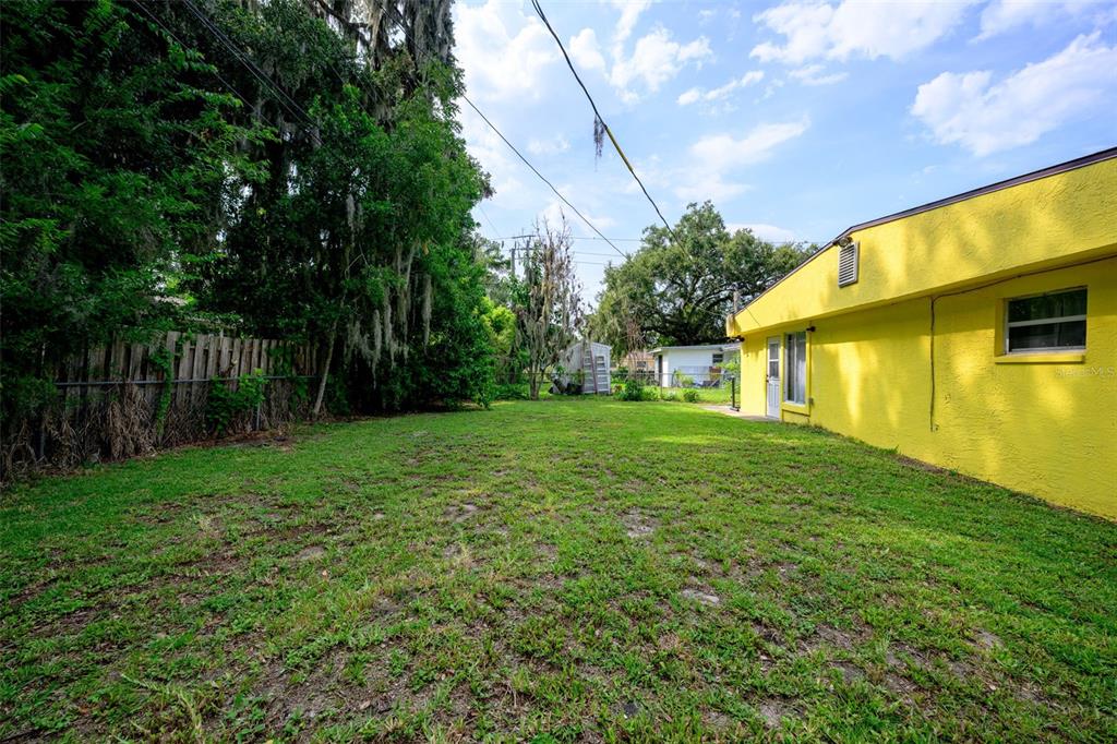 A bright yellow house exterior sits next to a grassy backyard with a wooden fence — 1003 CHEROKEE RANCH ROAD, HOLLY HILL, FL