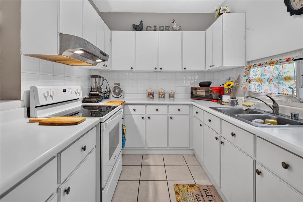 A white kitchen features white cabinets, tiled countertops, a stove, and a double-basin sink — B-21 MANSIONES DE CABO ROJO, CABO ROJO, PR
