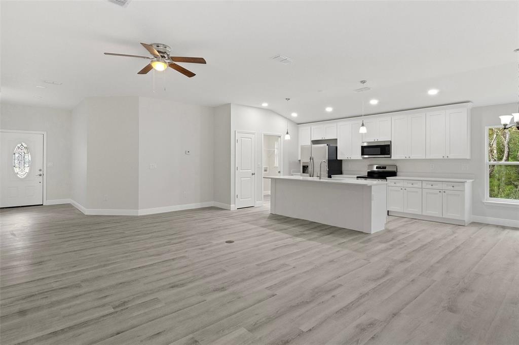 An open-concept kitchen and living area featuring white cabinets, a central island, and wood-look flooring — 1005 YALE LN, INVERNESS, FL