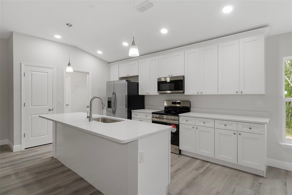 A modern kitchen features white cabinets, stainless steel appliances, a center island, and light flooring — 1005 YALE LN, INVERNESS, FL