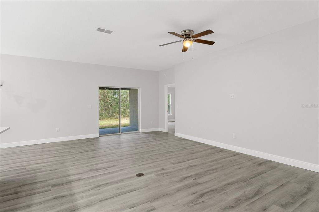 An empty living room with light gray walls, wood-look flooring, and a sliding glass door — 1005 YALE LN, INVERNESS, FL