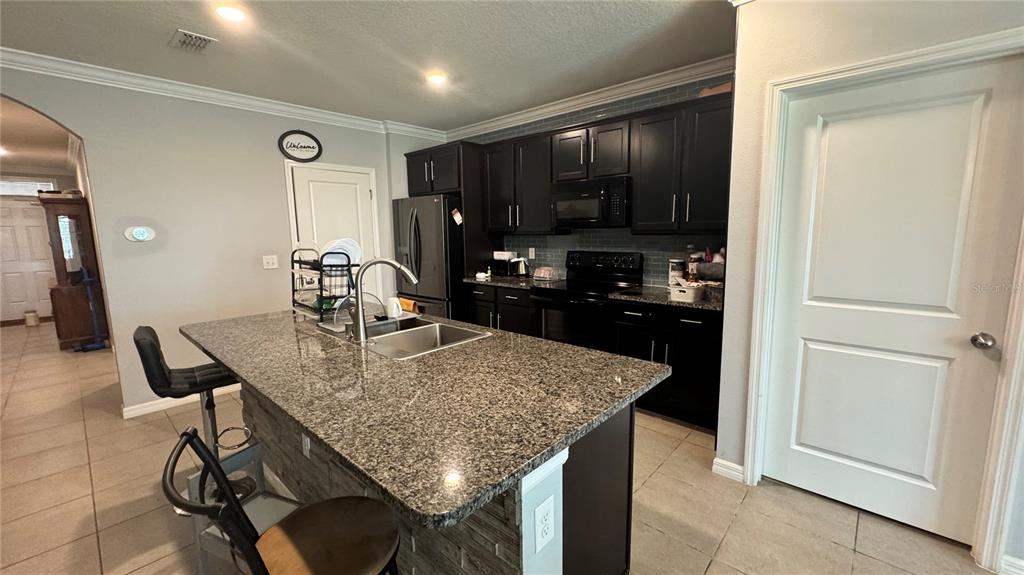 A kitchen features dark cabinets, granite countertops, a central island with a sink, and tile flooring — 259 HICKORY COURSE RADIAL, OCALA, FL