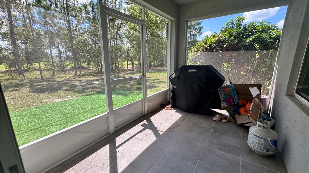 A screened-in patio features tiled flooring, a covered grill, and a view of trees — 259 HICKORY COURSE RADIAL, OCALA, FL