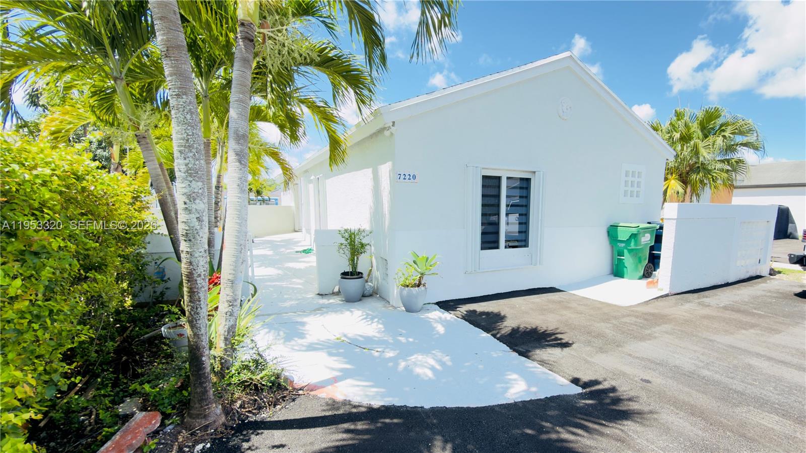A white single-story house exterior features a paved driveway, palm trees, and a green bin — 7220 SW 149th Ct, Miami FL 33193, MIAMI, FL