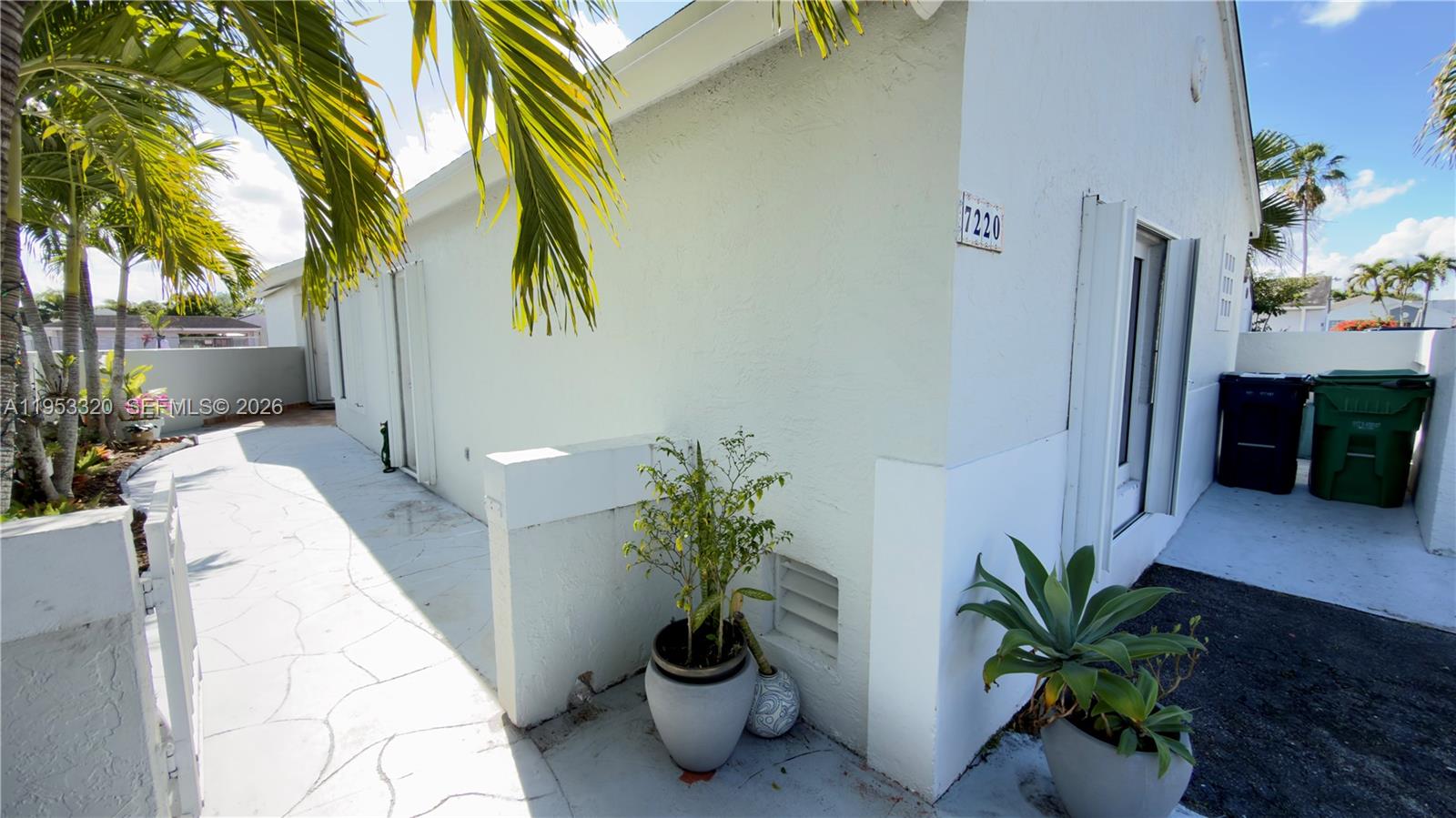 A white exterior wall features a house number, potted plants, and a paved walkway — 7220 SW 149th Ct, Miami FL 33193, MIAMI, FL