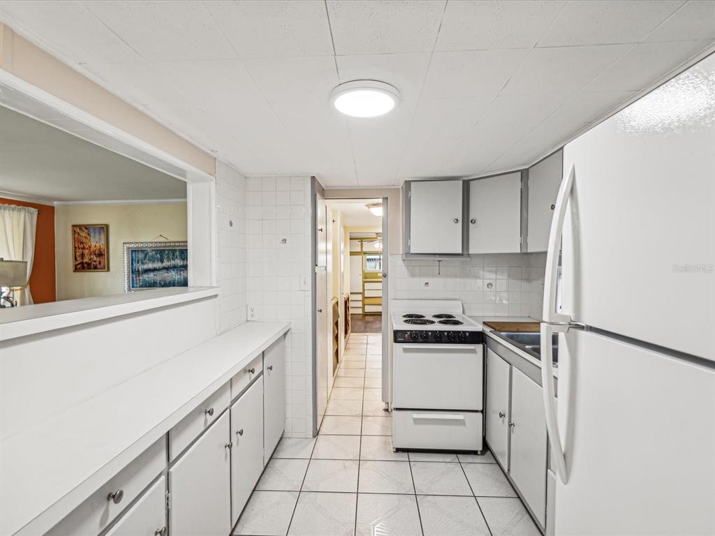 A kitchen features white cabinets, a white stove, tiled floors, and a pass-through window — 1940 SHADY COVE DRIVE, HOLIDAY, FL