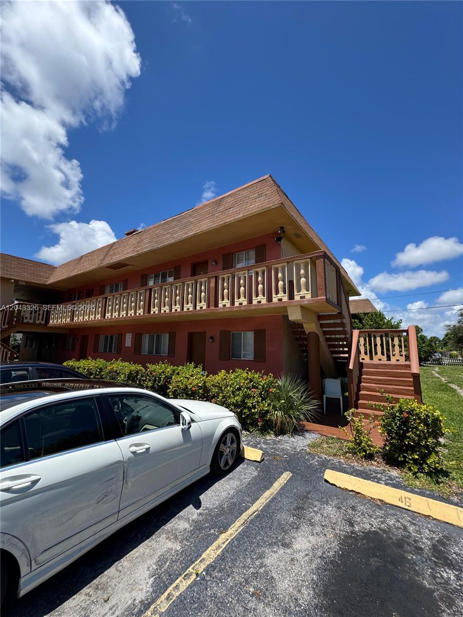 A two-story apartment building with a wooden balcony and exterior staircase under a blue sky — LAKE PARK, FL