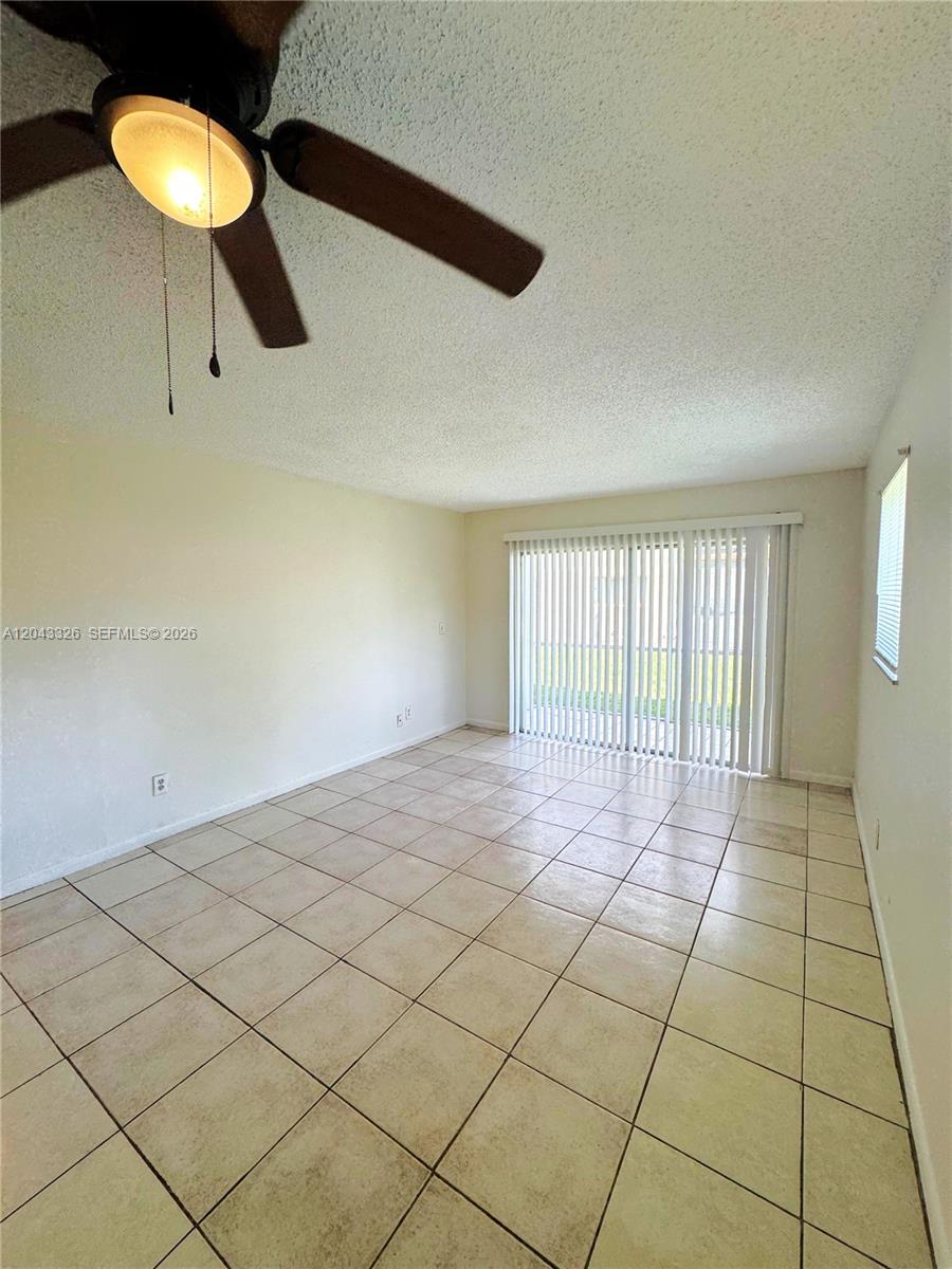 An empty room features beige tile flooring, a ceiling fan, and sliding glass patio doors — LAKE PARK, FL