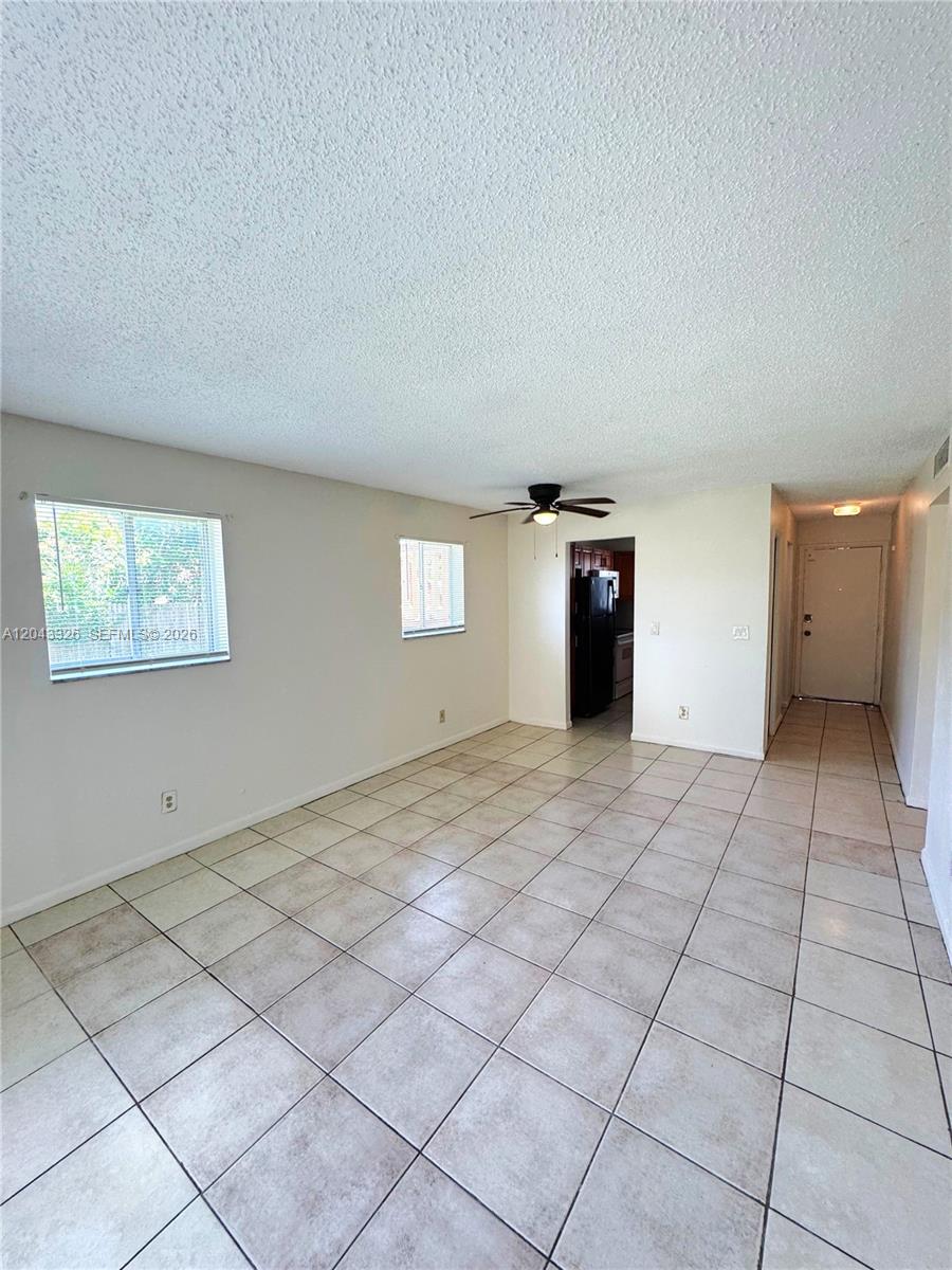 An empty living room features white walls, a ceiling fan, and light-colored tiled flooring — LAKE PARK, FL