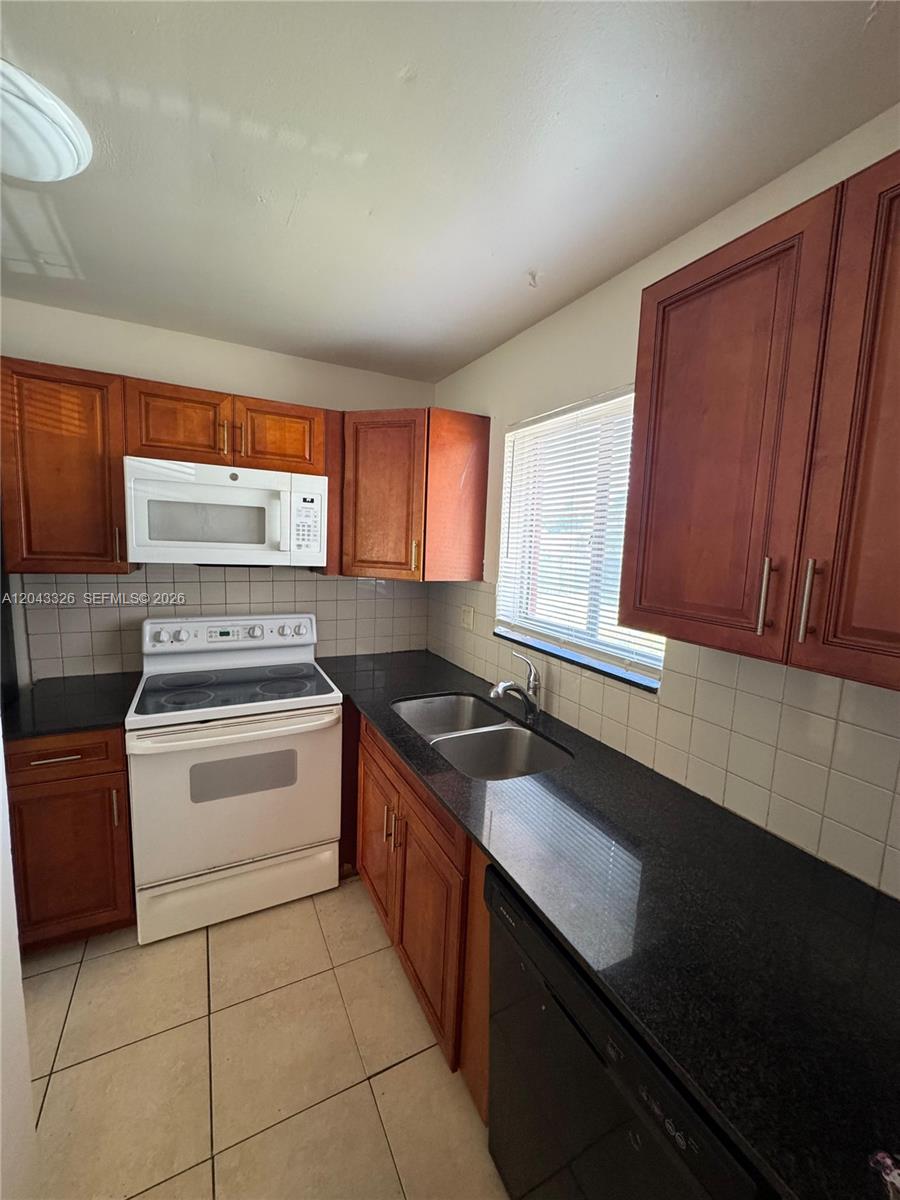A kitchen features wood cabinets, black countertops, white appliances, and a tiled backsplash — LAKE PARK, FL