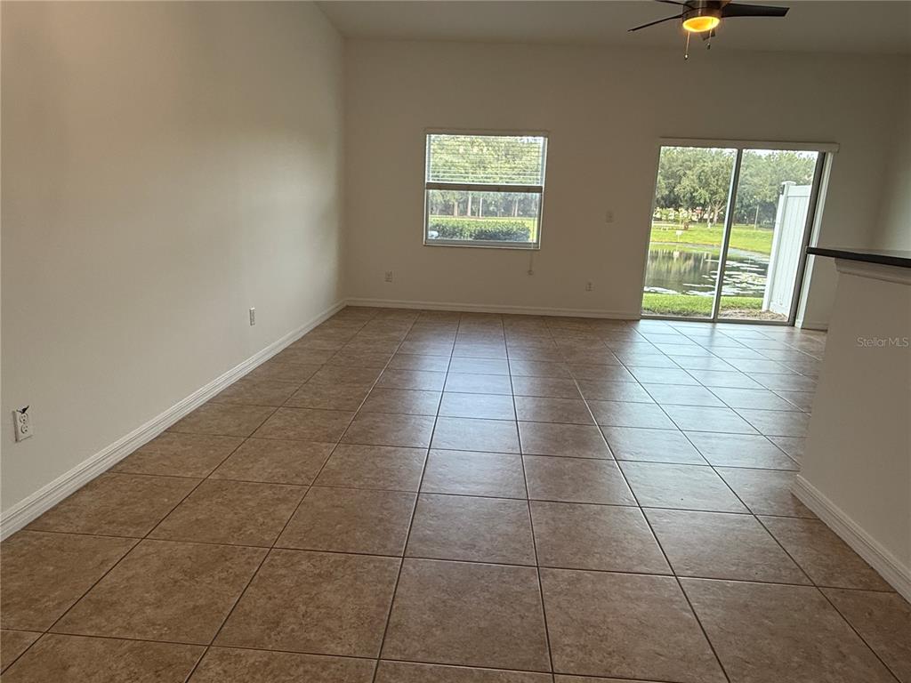 An empty room features beige tile flooring, a window, and sliding glass doors overlooking water — 12243 CITRUSWOOD DRIVE, ORLANDO, FL